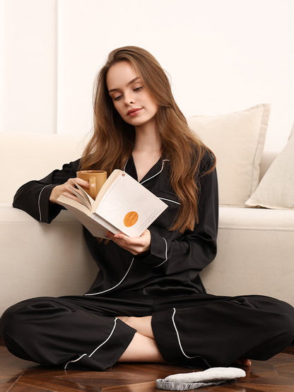 Woman in black pajamas reading a book on a white couch.